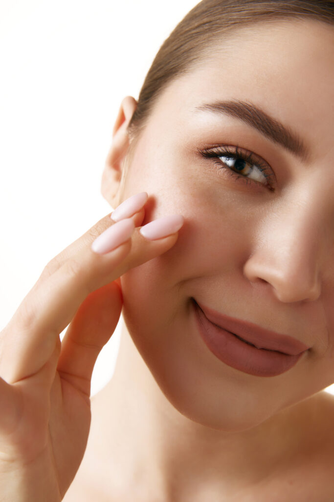 A young woman touching her cheek with healthy glowing skin and natural makeup post biostimulators theory