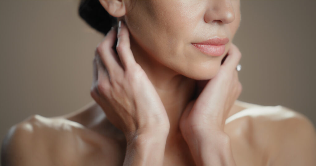 A woman touching her face and neck, representing smooth glowing and anti aging skincare concepts.