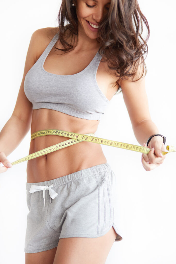 Fit woman measuring her waist representing weight loss and body wellness